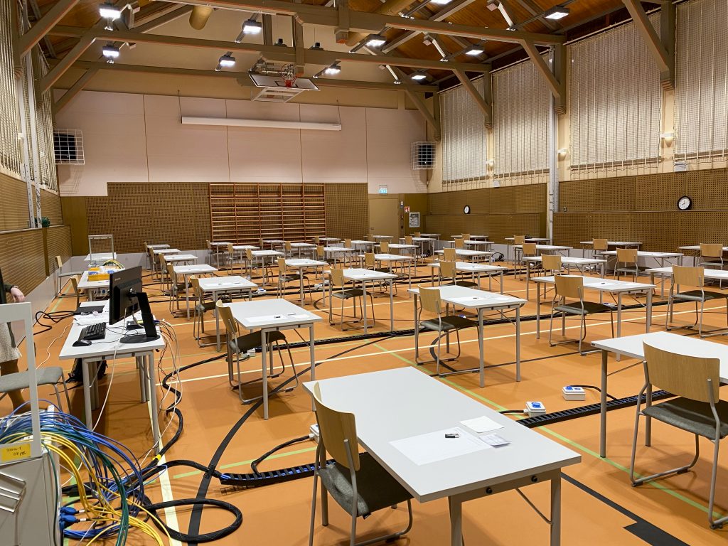 En gymnastiksal fylld av bord och stolar med elektronisk utrustning på golven