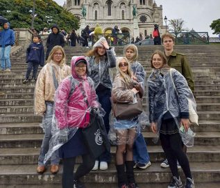 Ungdomar och vuxna på en trappa i Paris, det regnar